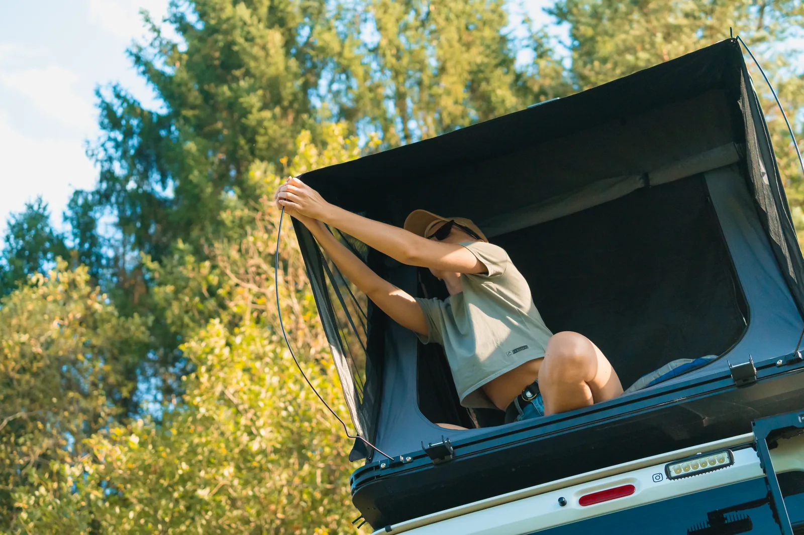 Woman setting up an open SNAILER roof tent on a vehicle